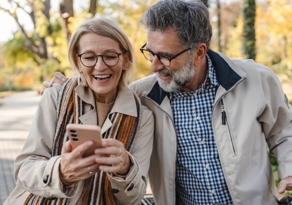 Senior couple walking outside smiling and looking at phone.