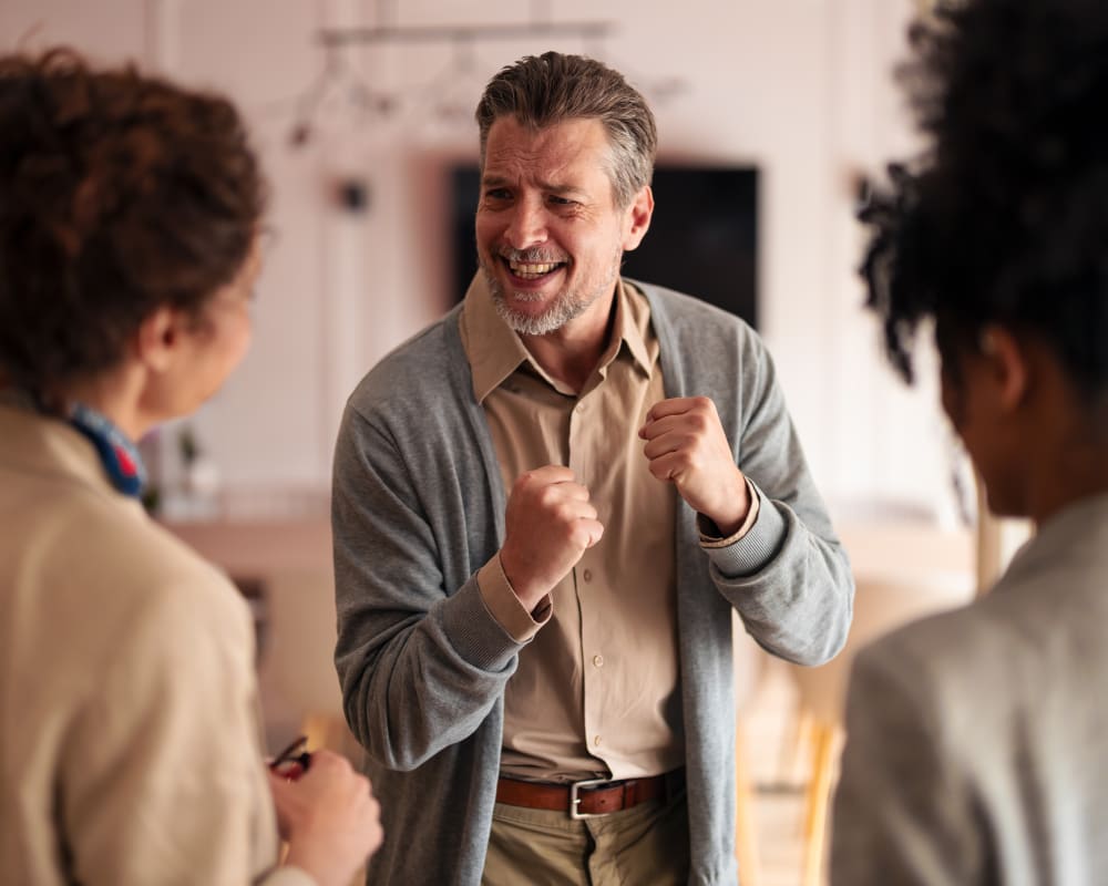 Man excited holding hands up and smiling while talking to two women.