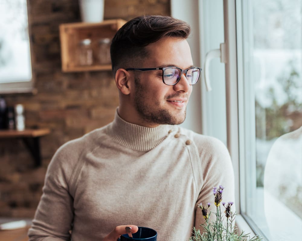 Young man with glasses smiling and looking out window.